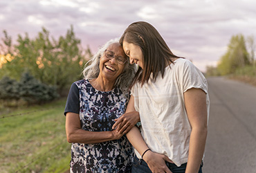 A beautiful senior mom of pacific island descent is walking outdoors with her adult thirty something year old daughter. They are enjoying each others company and soaking in the gorgeous, colorful, sunset.